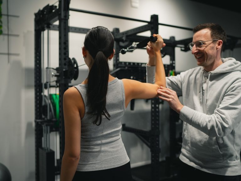 Eine Frau mit braunen Haaren wird beim Training von einem Mann unterstützt.