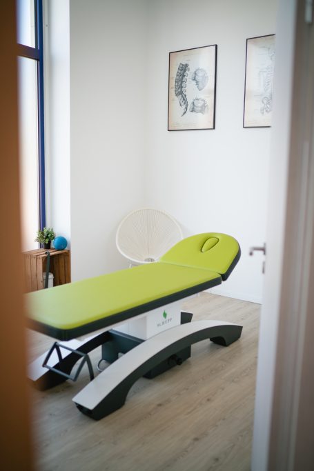 Behandlungsraum mit einer grünen Liege und Kunstwerken an den Wänden.