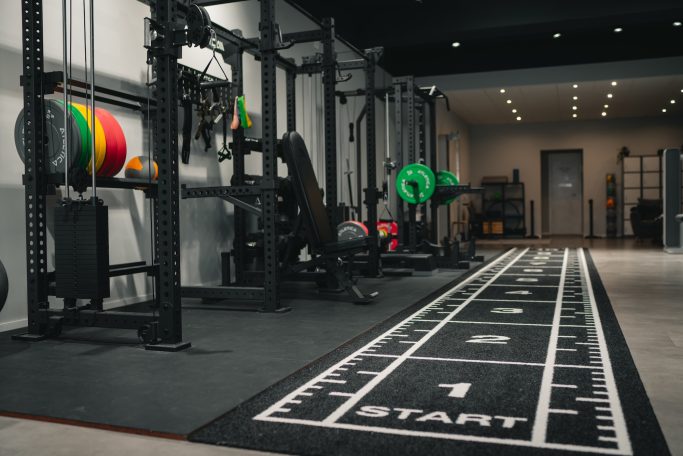 Moderne Fitnessspielstätte mit Gewichten und Trainingsgeräten, Startlinie auf dem Boden.