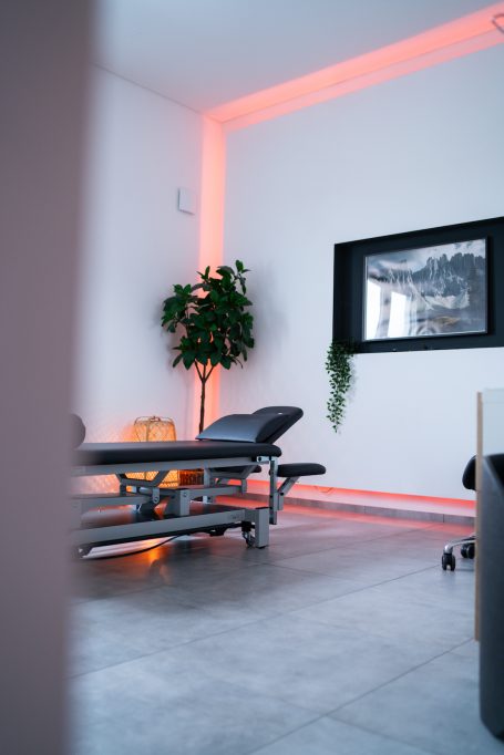 Behandlungsraum mit einer Liege, Pflanzen und sanftem, rosafarbenem Licht.