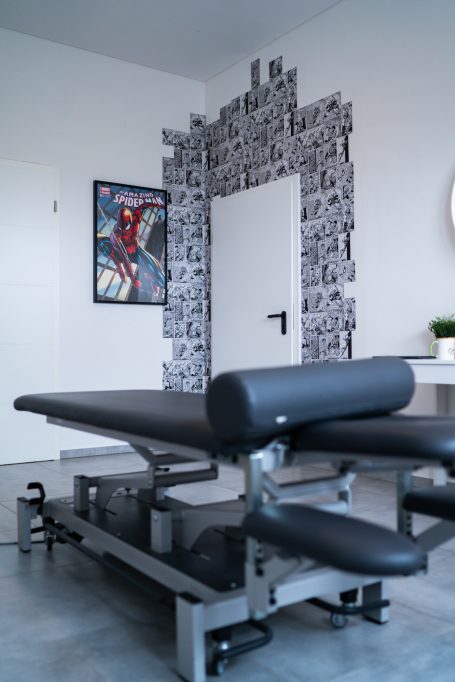 Behandlungsbank in einem modernen Raum mit schwarzer Wanddekoration und einem Plakat.