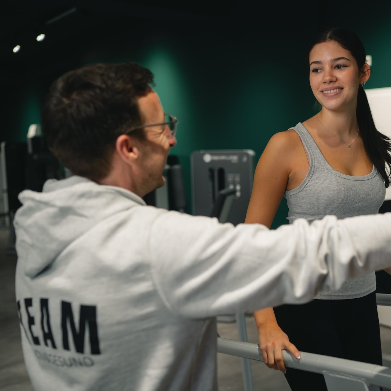 Junger Mann und Frau lächeln sich im Fitnessstudio an, während sie trainieren.